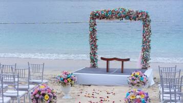 Decoração de casamento na praia, com arco de flores, cadeiras e palco.