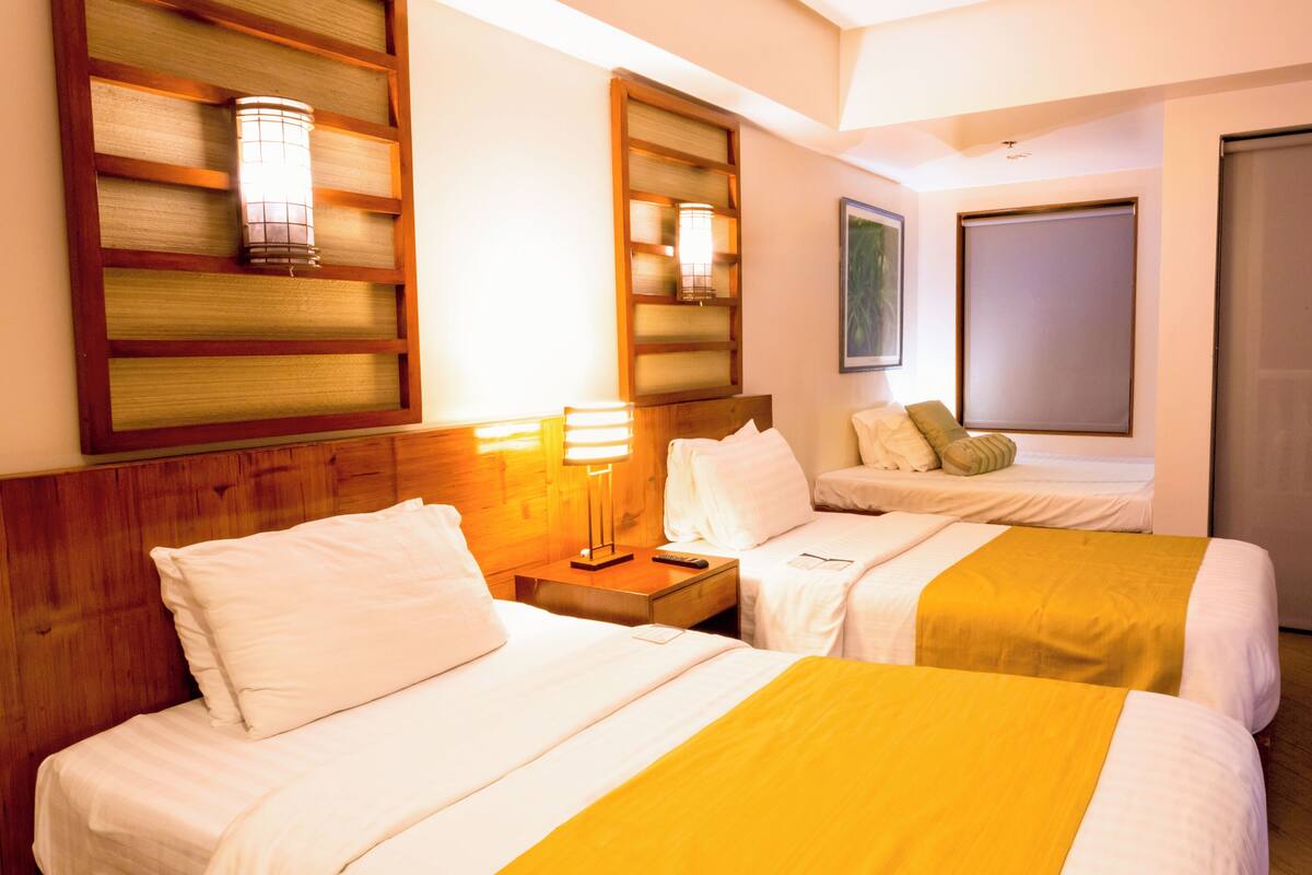 A hotel room with two beds, a wooden headboard, a nightstand with a lamp, and a large window with a view.