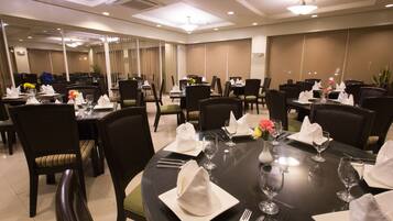 A hotel dining area with multiple round tables set for dining, each with chairs, plates, cutlery, and glasses.