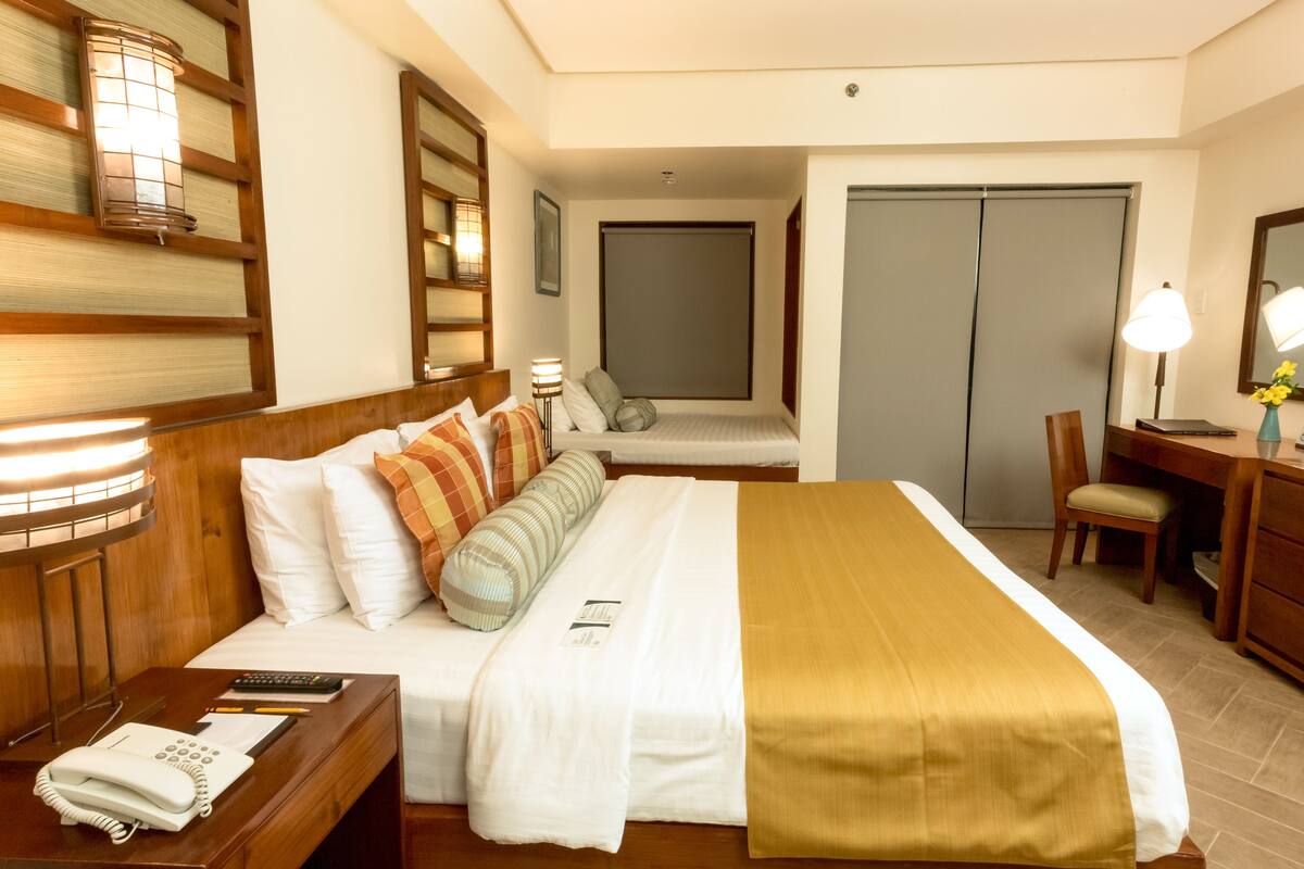 A hotel room with a bed, bedside table, desk, chair, and a wardrobe.