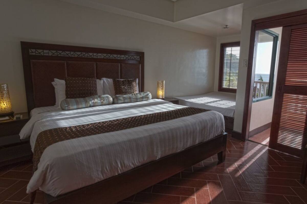 A spacious bedroom with a large bed, two bedside tables with lamps, and a view of the outside through a sliding door.