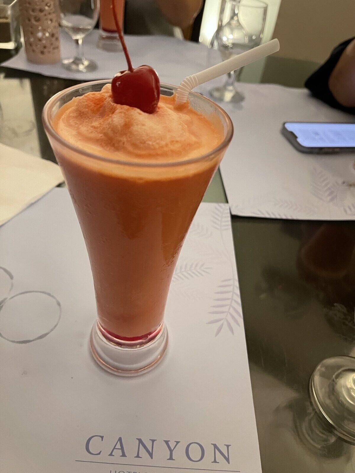A tall glass of a pink beverage with a cherry on top, placed on a table with a menu titled "CANYON".