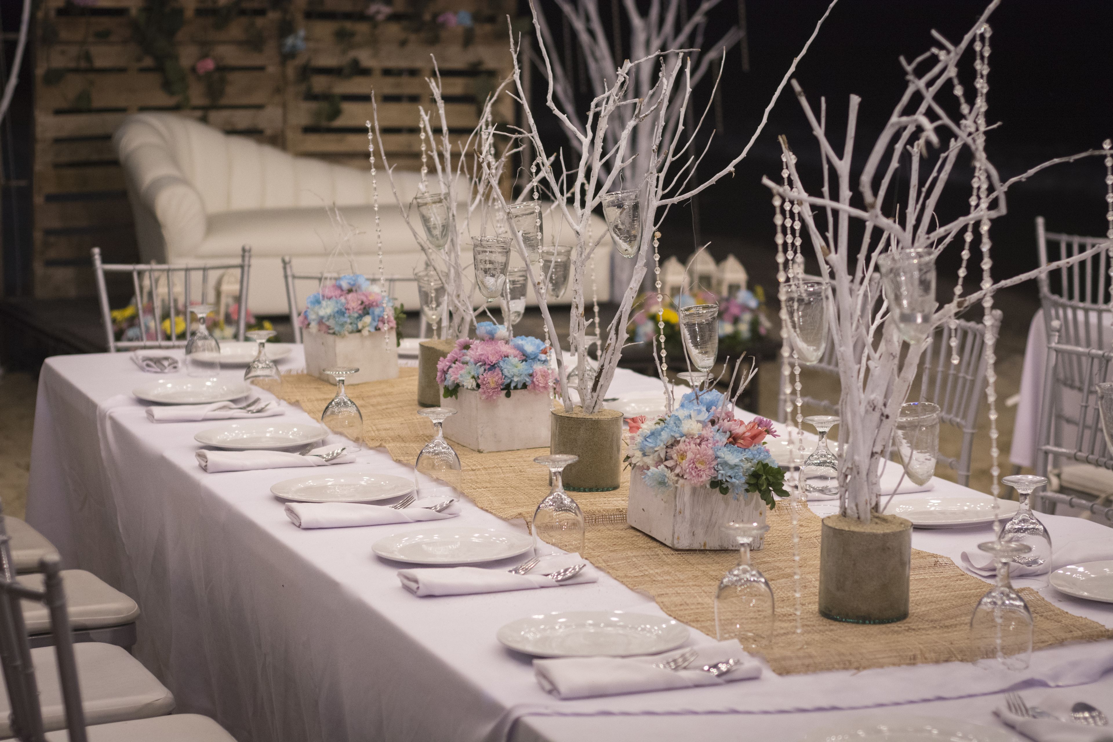 A long dining table set with white plates, silverware, and glassware, adorned with floral arrangements in clear glass vases.