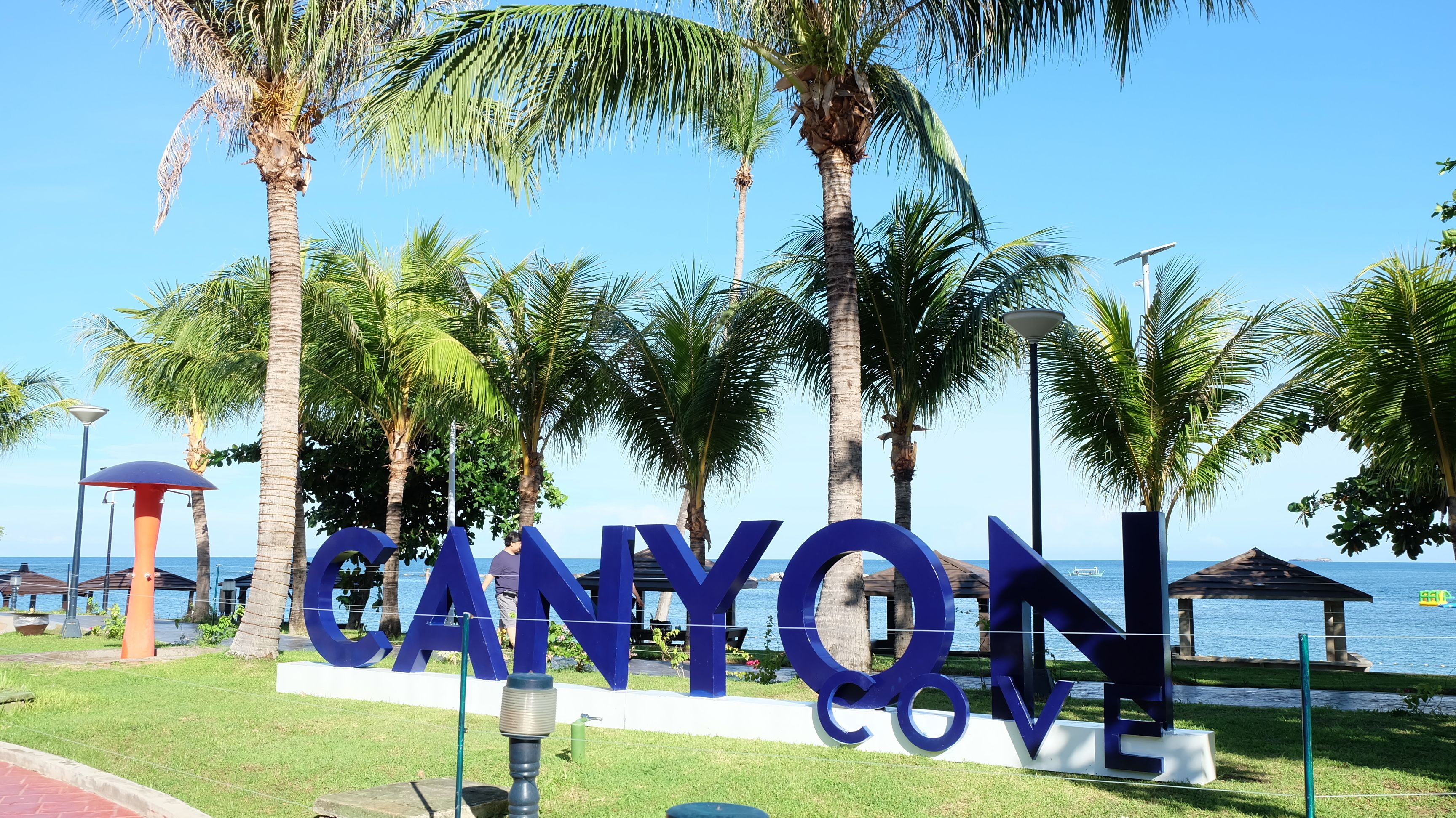 A sign with the word "CANYON" in large blue letters, surrounded by palm trees and a view of the sea.