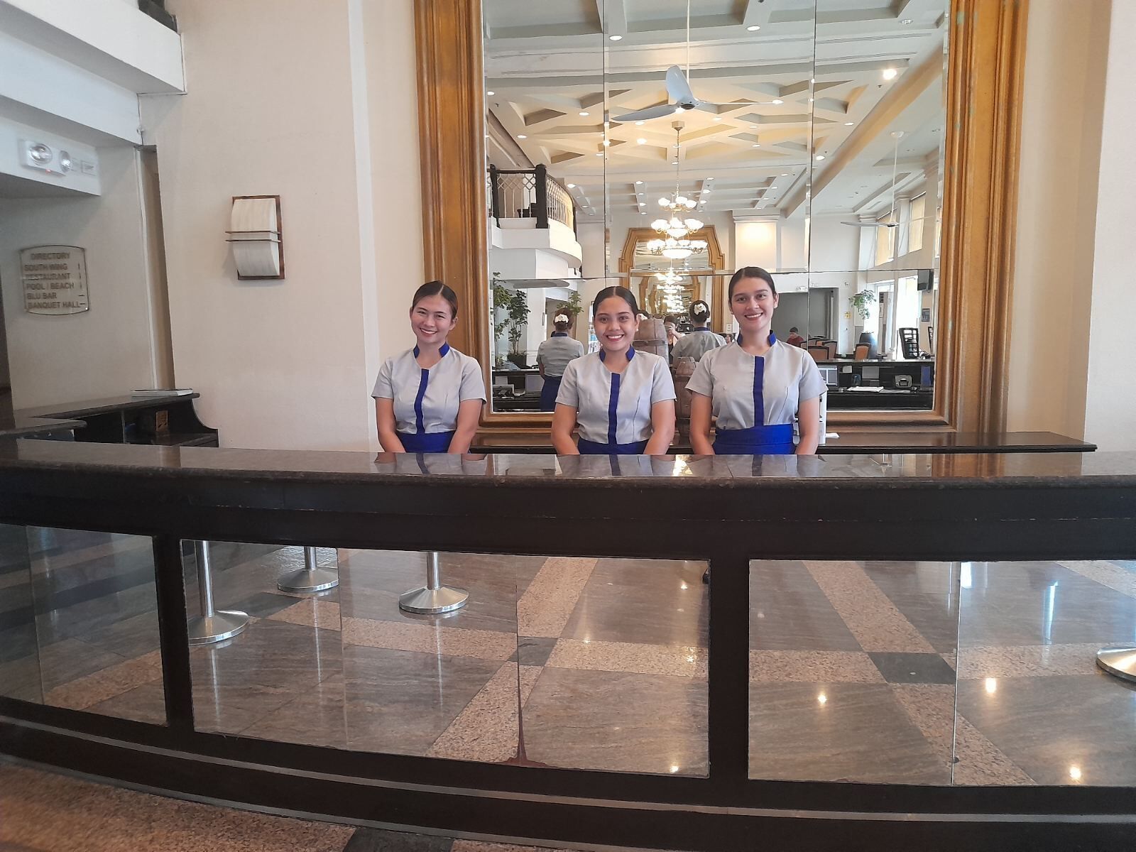 A reception area with a marble floor, a reception desk, and a large mirror reflecting the interior.