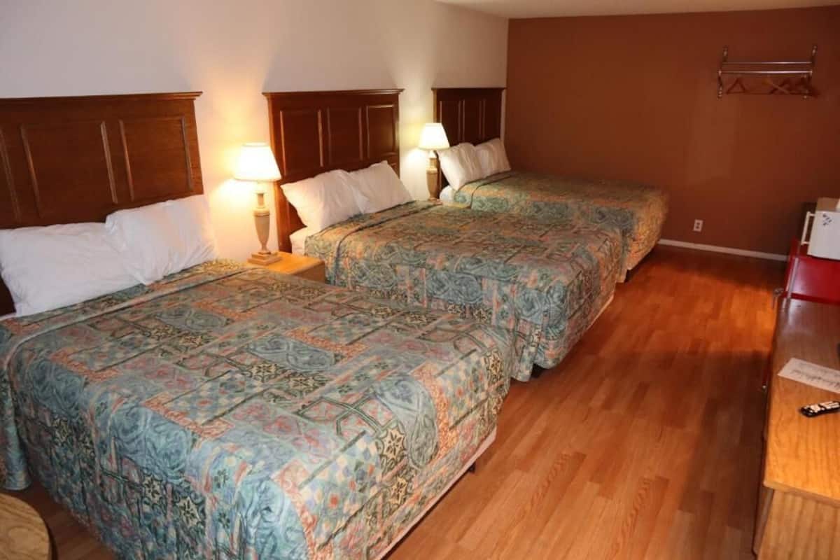 Ein Hotelzimmer mit zwei Betten, Holz-Kopfteilen, gemusterten Bettdecken, Nachttischlampen und Holzboden.