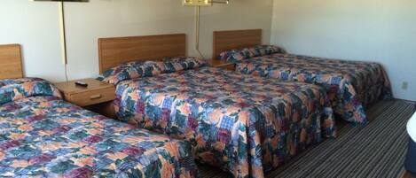 A hotel room with three beds, each with floral-patterned bedding, a wooden headboard, and a nightstand with a lamp.