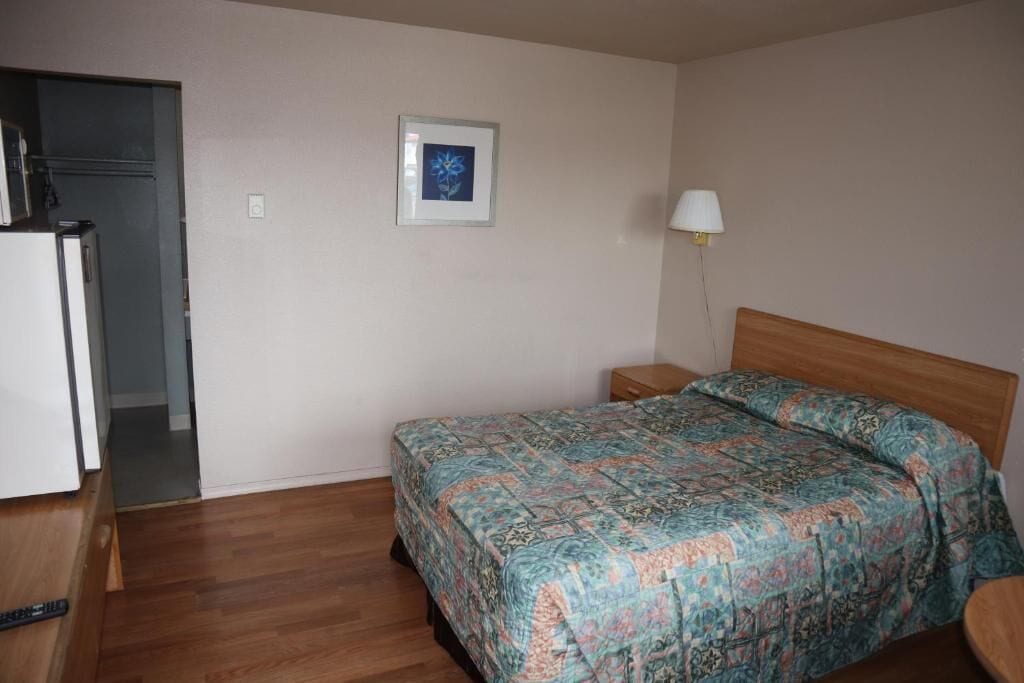 Quarto com cama, mesa de cabeceira, abajur e porta para outro cômodo.