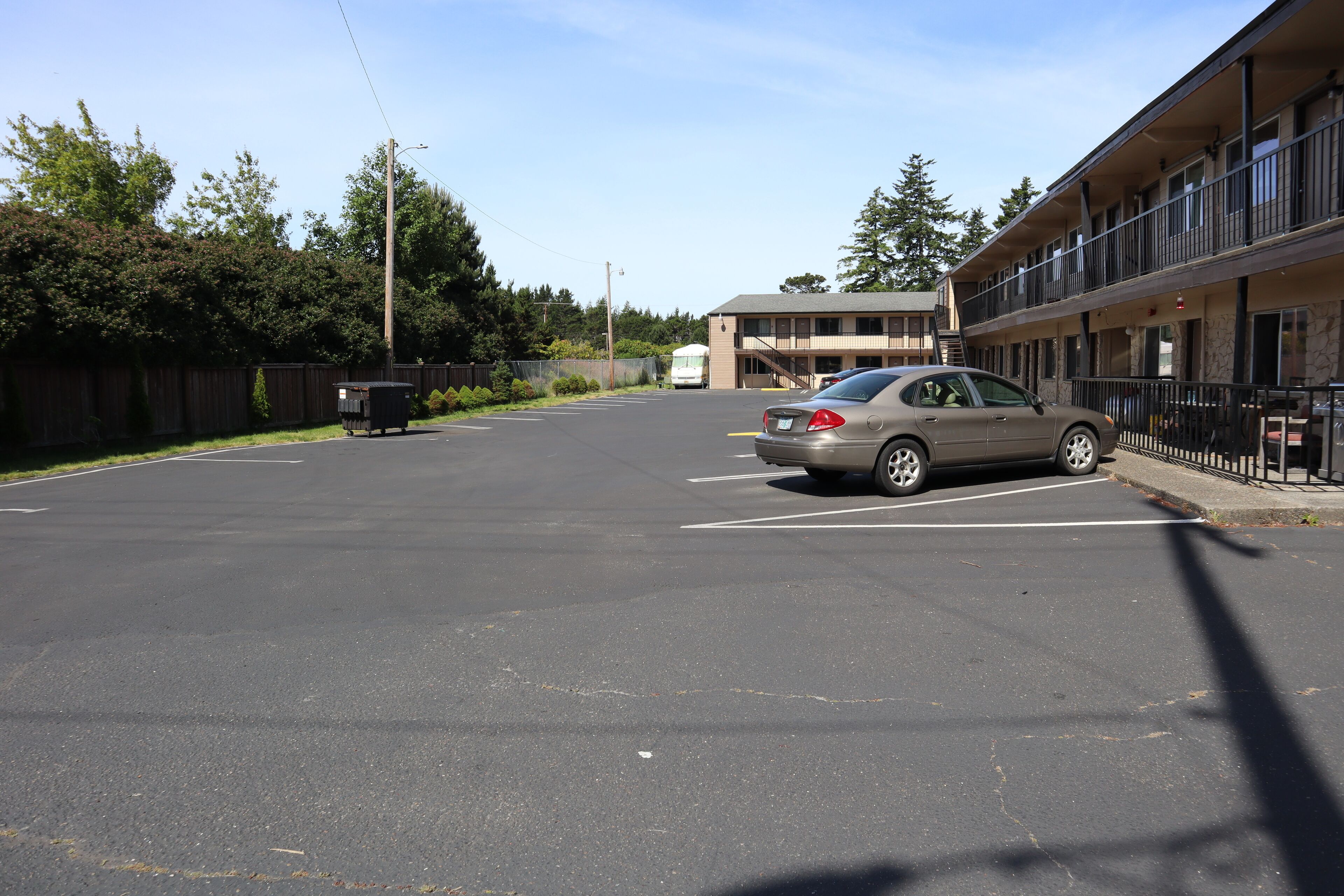 A parking lot with a car, a dumpster, and a building with balconies.
