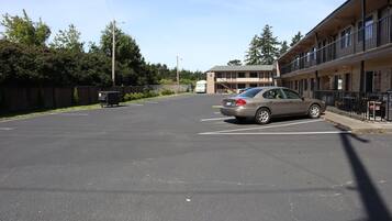 A parking lot with a car, a dumpster, and a building with balconies.