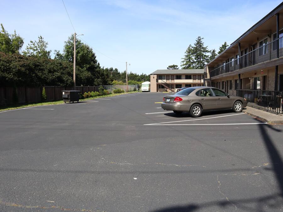 A parking lot with a car, a dumpster, and a building with balconies.