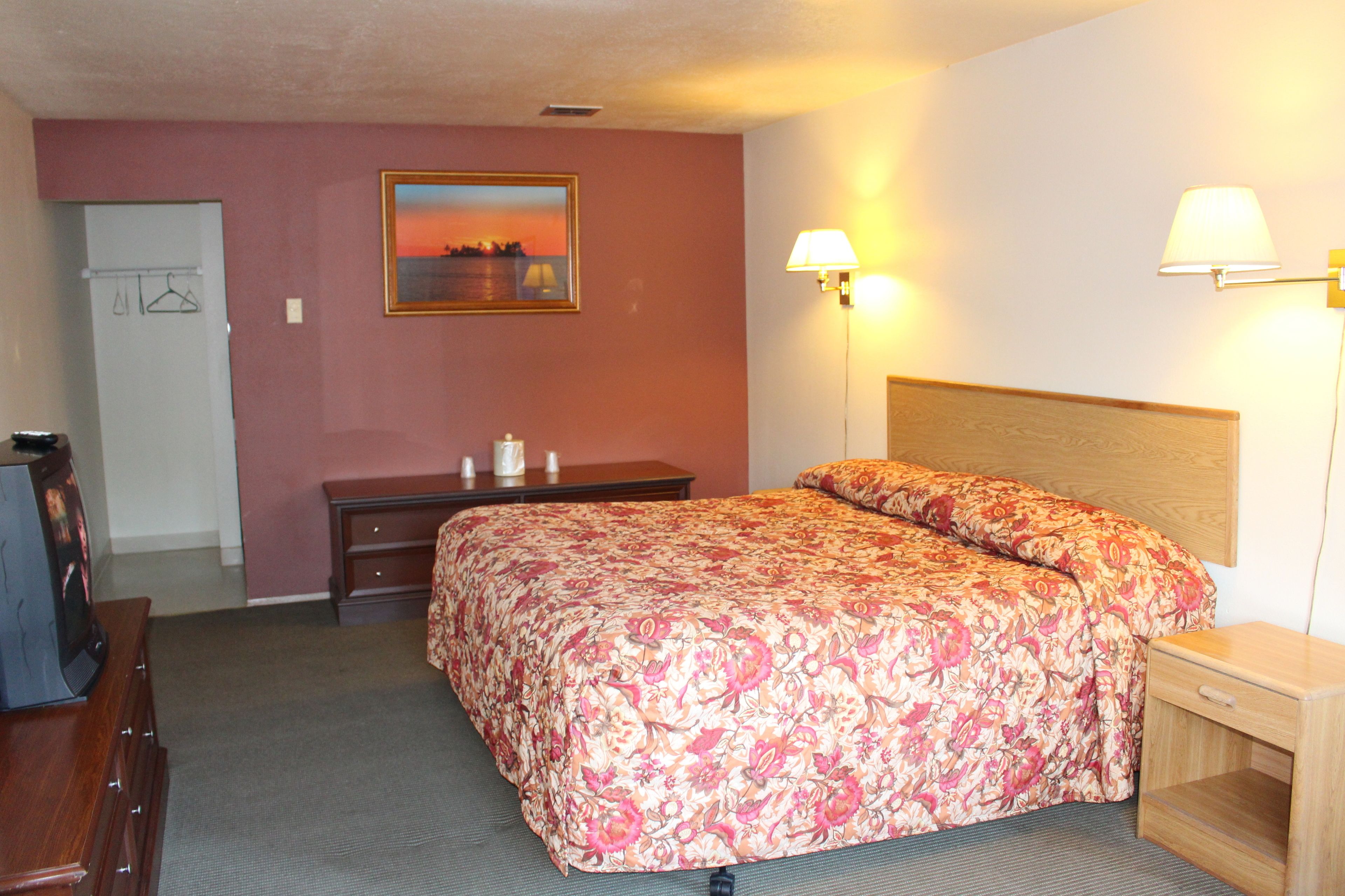A hotel room with a bed, a desk, a chair, a dresser, and a lamp.