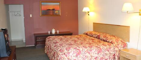 A hotel room with a bed, a desk, a chair, a dresser, and a lamp.