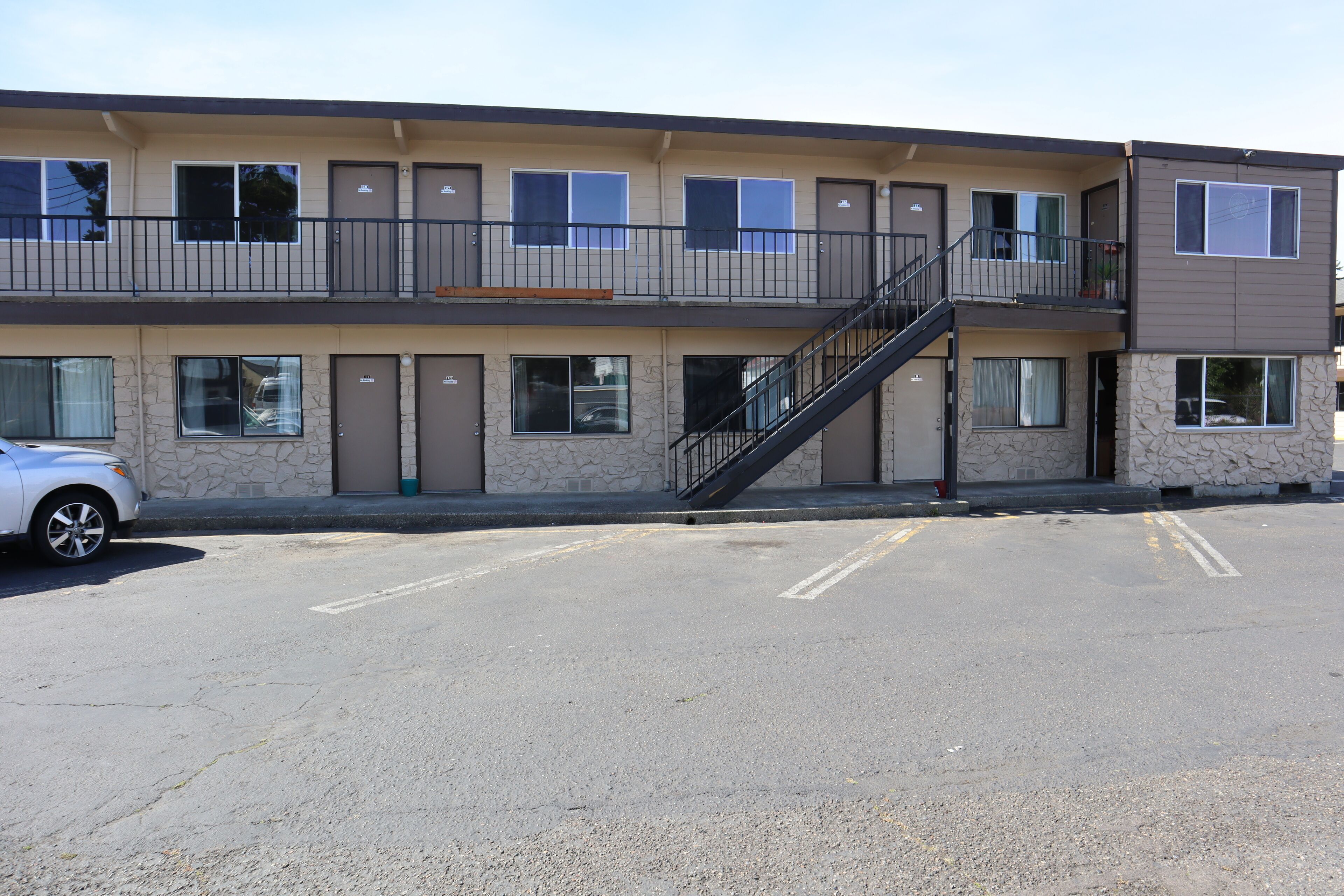 A multi-story motel with a central staircase, individual rooms on each floor, and a parking lot in front.