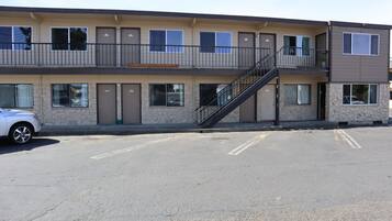 A multi-story motel with a central staircase, individual rooms on each floor, and a parking lot in front.