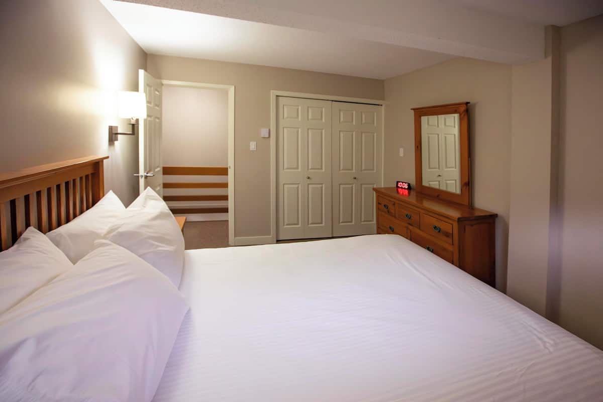 Una habitación de hotel con cama, cómoda, espejo, puerta y lámpara.