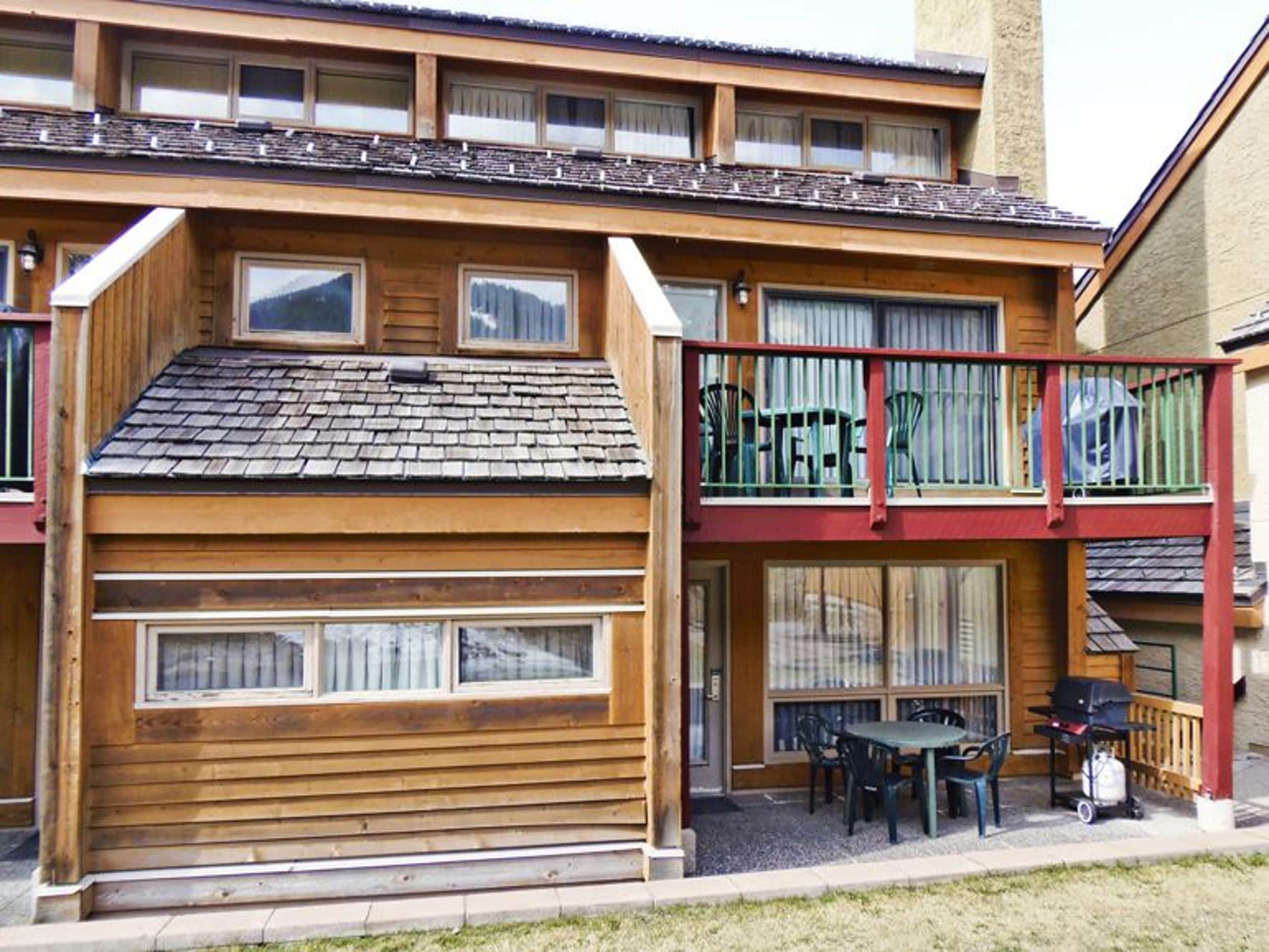 Un edificio de madera de dos pisos, con balcón, ventanas grandes y mesas al aire libre.
