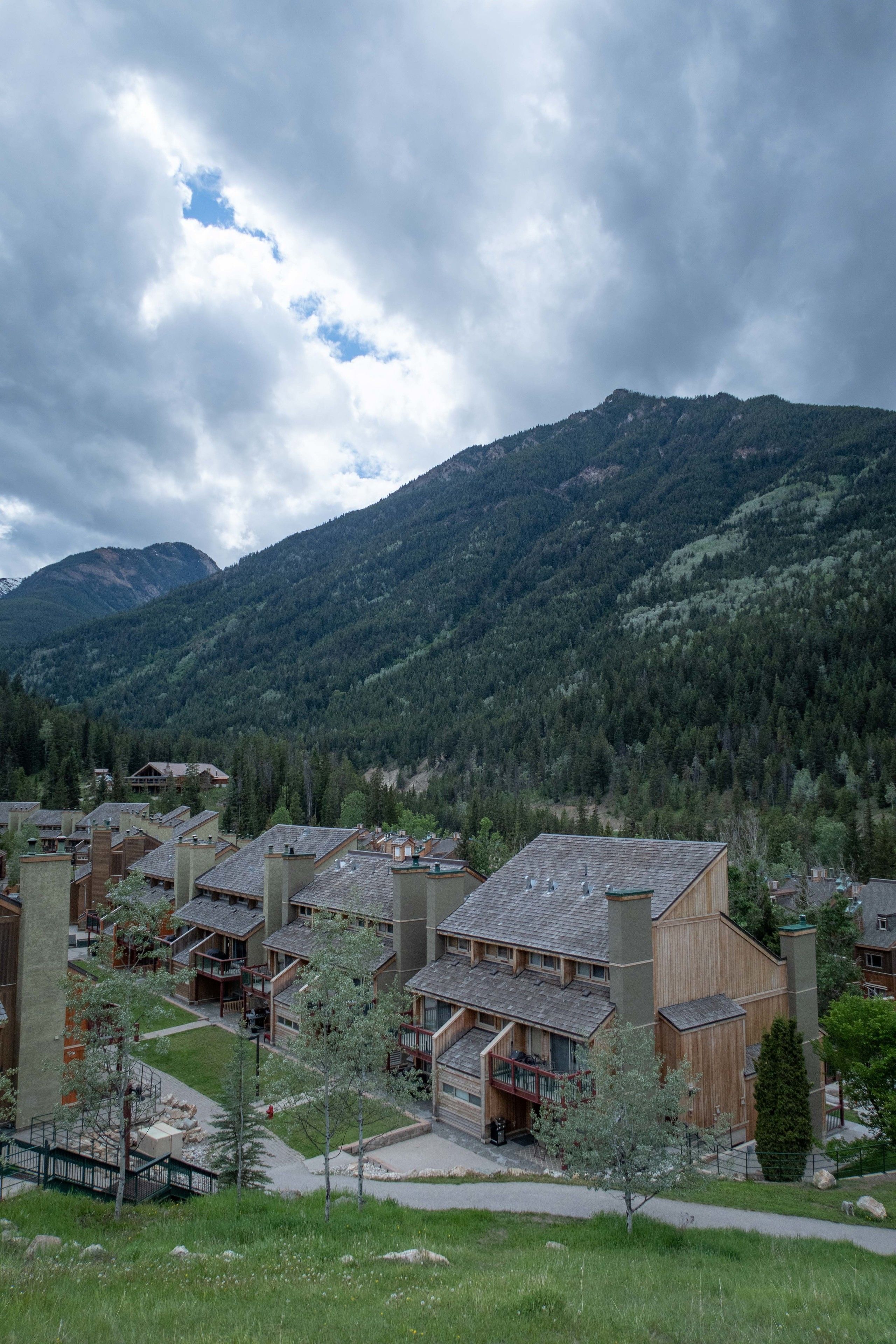 Un chalet de montagne composé de plusieurs bâtiments en bois, doté d’une cour centrale et offrant une vue sur les montagnes environnantes, couvertes de forêts.