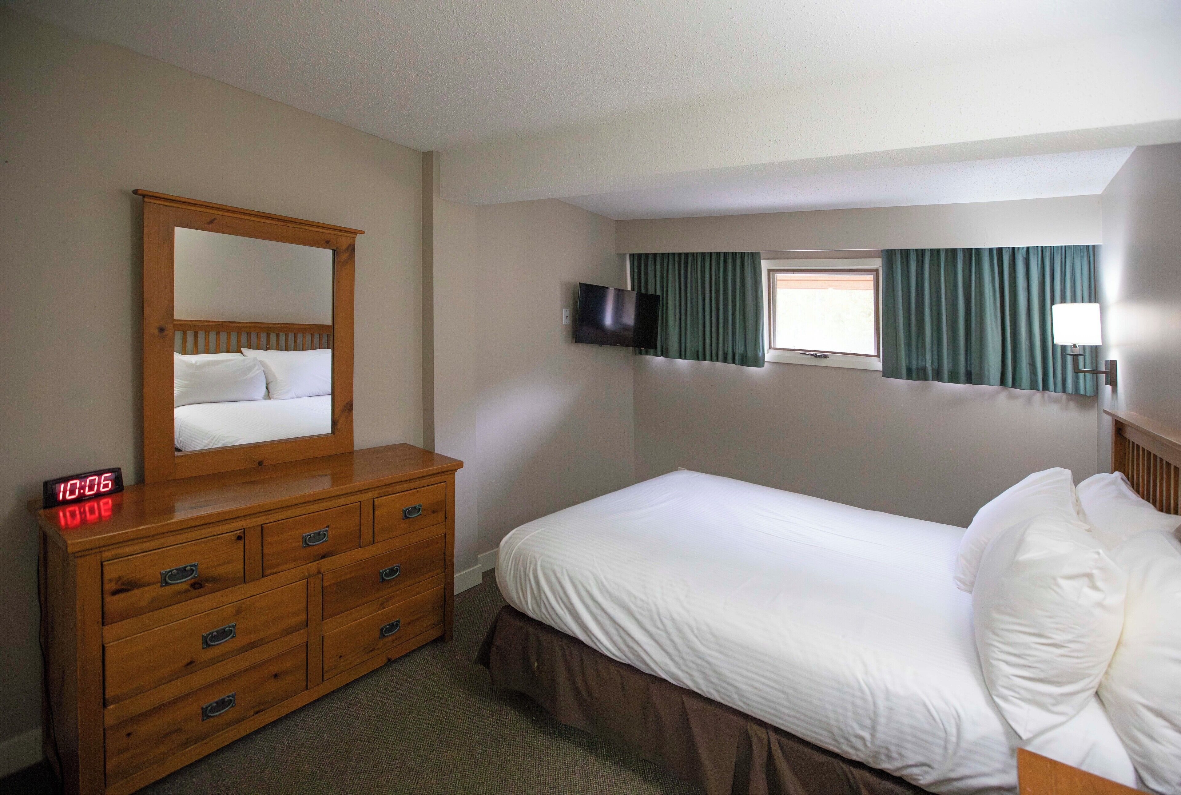A hotel room with a bed, a dresser, a mirror, a TV, and a window with curtains.