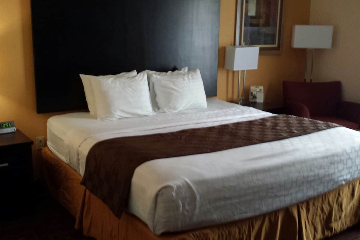 A hotel room with a large bed, a nightstand with a clock, and a red chair.