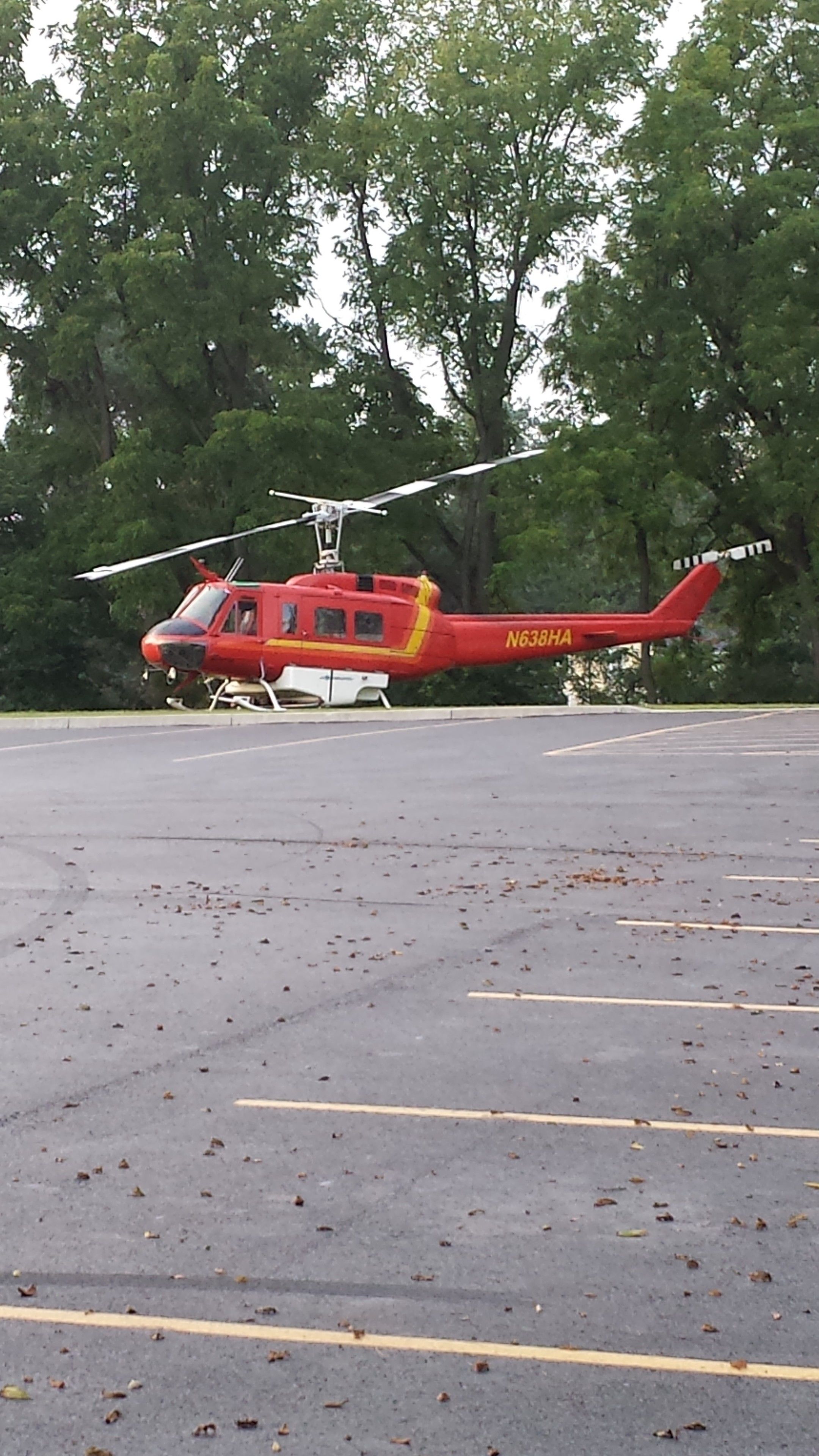 A red helicopter with the registration N638HA parked in a parking lot with trees in the background.