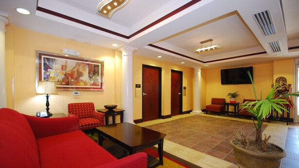 A hotel lobby with a red sofa, a coffee table, a painting on the wall, a television, and a potted plant. - Paradise Inn & Suites (Towanda)