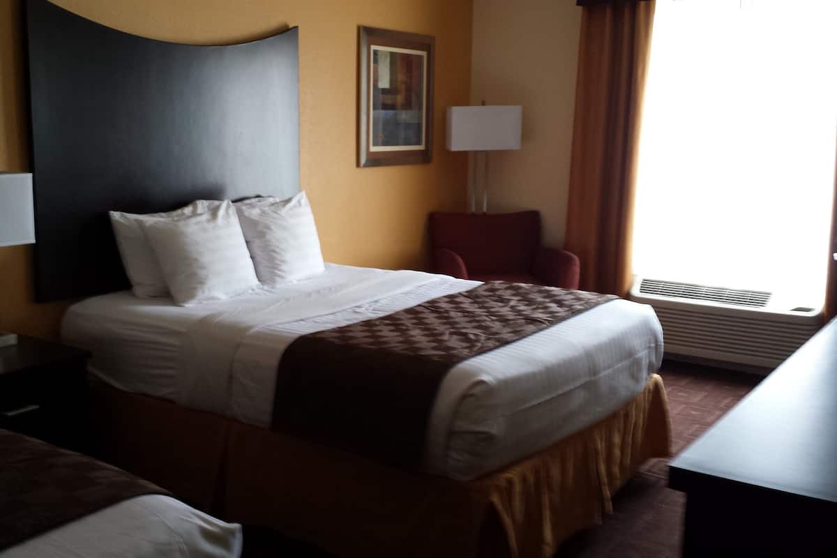 A hotel room with a bed, a chair, a desk, and a lamp.