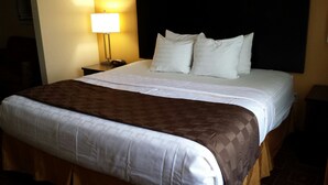 A neatly made bed with a white and brown bedspread, a black headboard, and two white pillows. There is a bedside lamp on the left side of the bed. - Paradise Inn & Suites (Towanda)
