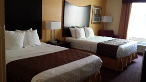A hotel room with two beds, a nightstand, a lamp, and a window with curtains.