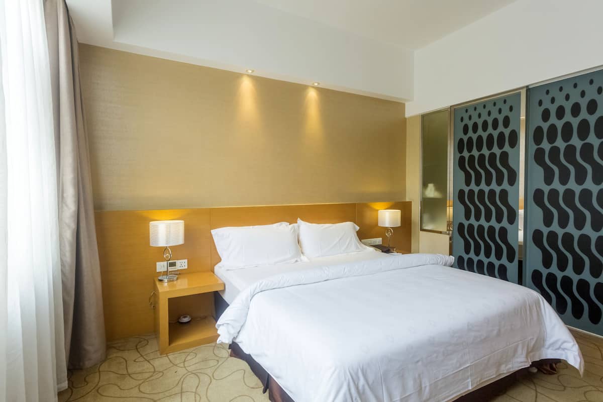 Une chambre d’hôtel avec un grand lit, deux lampes de chevet, une table de chevet en bois et un papier peint à motifs.