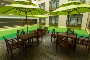 An outdoor patio area with wooden tables and chairs, green umbrellas, and potted plants. - Metropolo Guangzhou Wanda Plaza Hotel (Guangzhou)