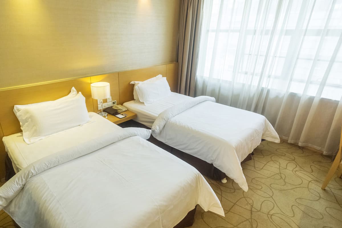Une chambre d’hôtel avec deux lits simples, une table de chevet avec une lampe, un téléphone et une petite table avec un carnet et un stylo.