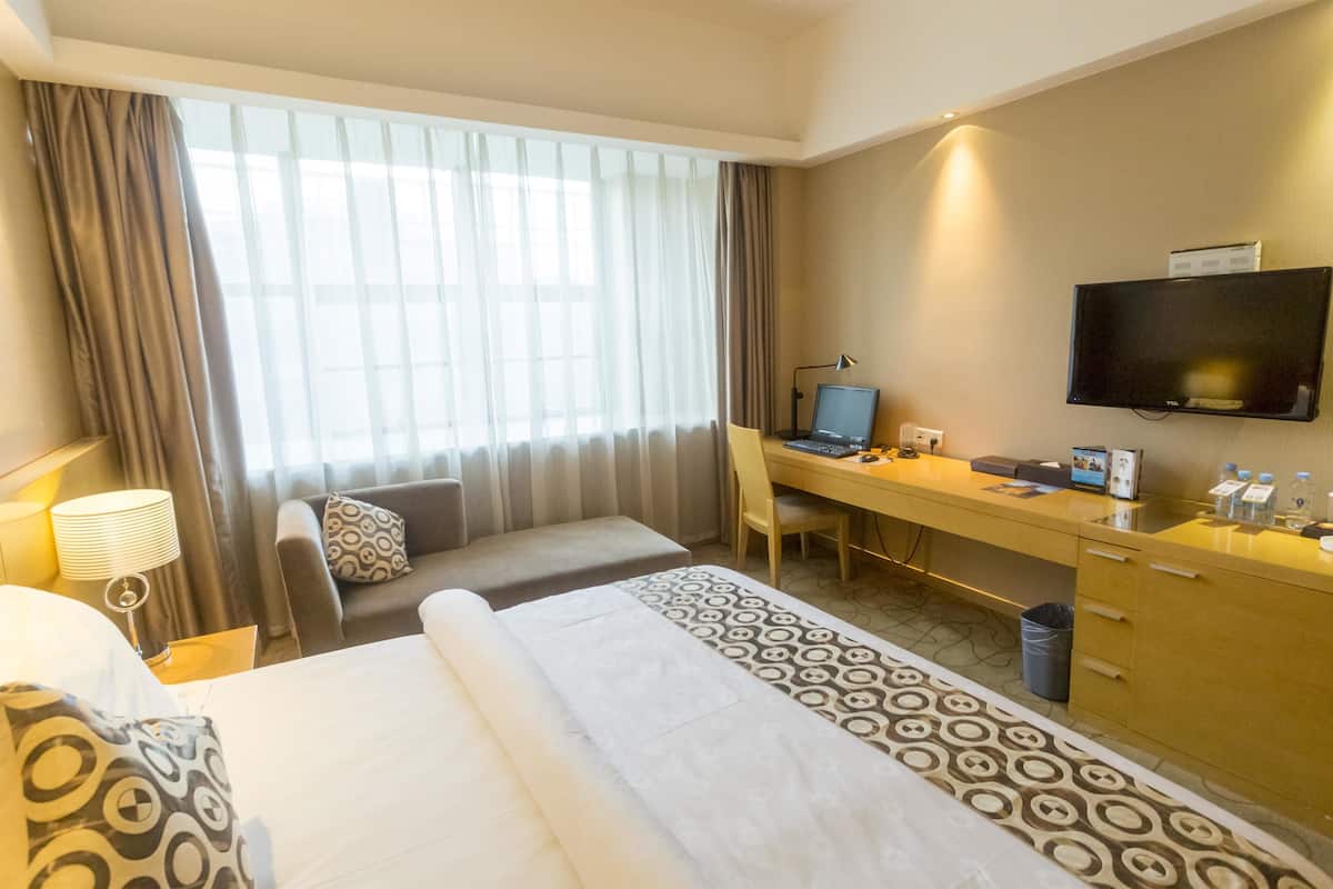 Une chambre d’hôtel avec un lit, un bureau avec un ordinateur, une télévision et une fenêtre avec des rideaux.