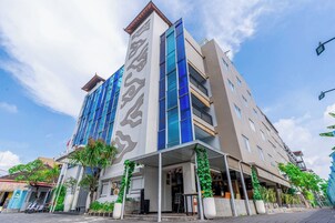Un hotel de varios pisos con diseño moderno, que cuenta con amplios ventanales y un elemento vertical destacado en la fachada.