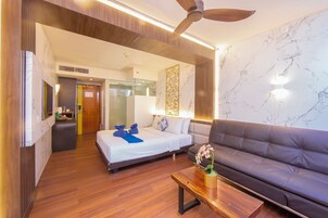 Habitación de hotel con cama, sofá, una mesita, ventilador de techo y pared de mármol.