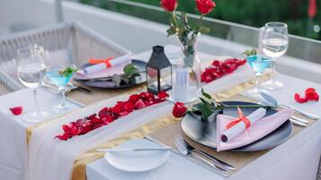Mesa posta com toalhas brancas, pétalas de rosas vermelhas e uma vela.