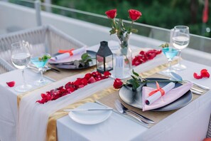 Una mesa dispuesta con manteles blancos, pétalos de rosa roja y una vela.