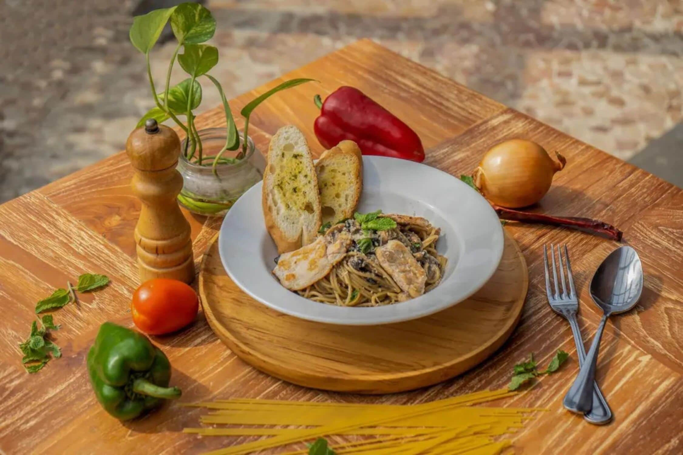 A wooden table with a plate of pasta, bread, and vegetables.