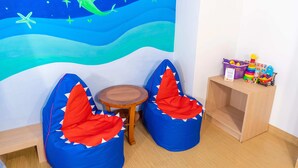 A room with two shark-themed bean bags, a small wooden table, and a wall mural of an underwater scene. - Kuta Beach Hotel (Kuta)