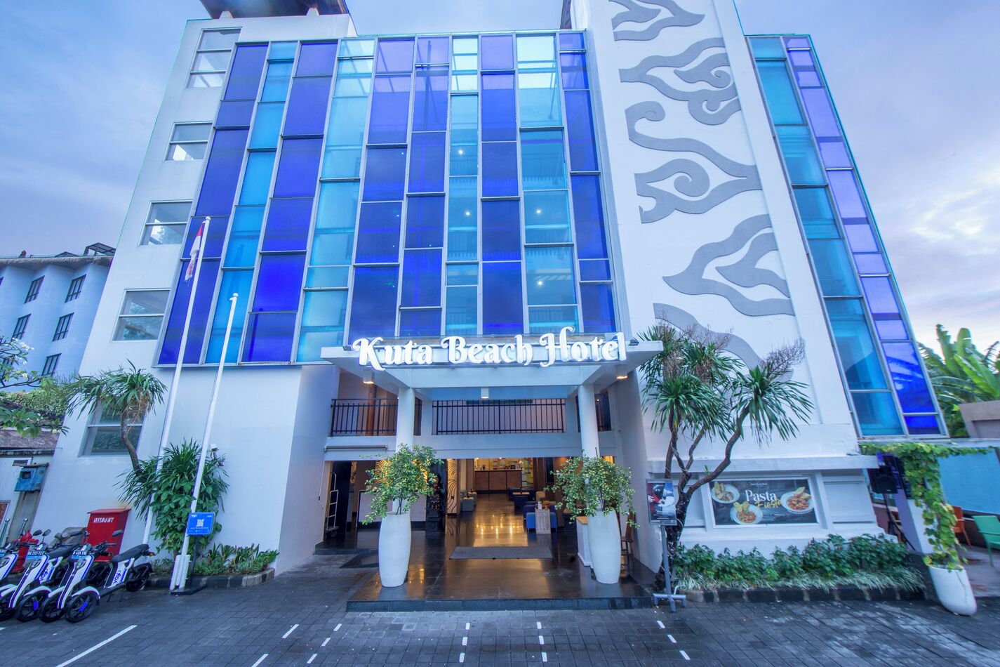 A hotel with a modern facade, large windows, and a sign reading 'Kuta Beach Hotel'.