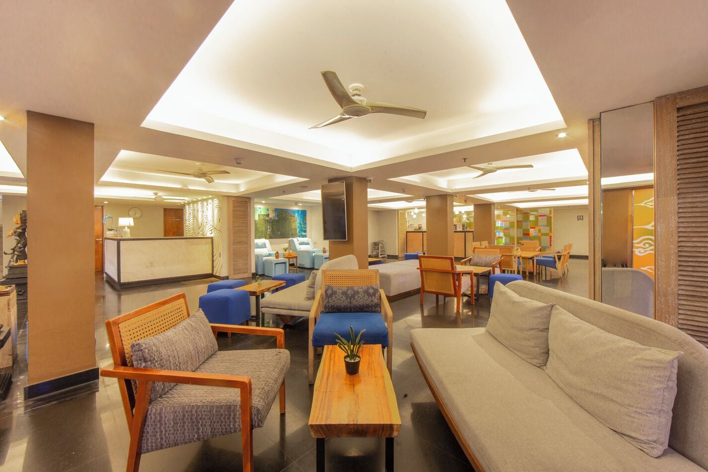 A hotel lobby with seating areas, a reception desk, and a ceiling fan.