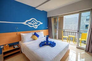 A hotel room with a bed, a nightstand, a digital clock, a window with curtains, and a balcony with yellow chairs.