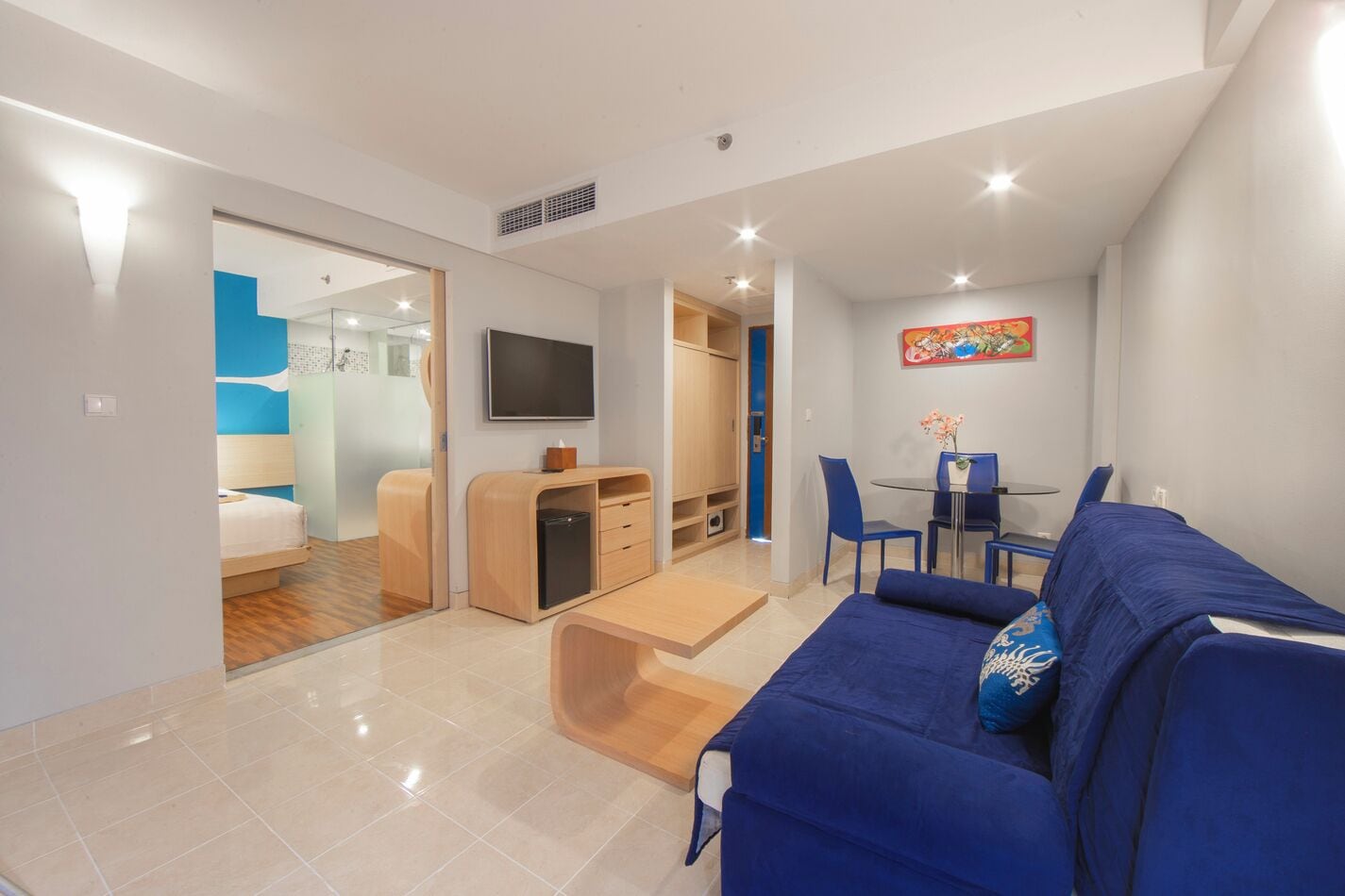 A modern living room with a blue sofa, a flat-screen TV, and a dining area with a table and chairs.