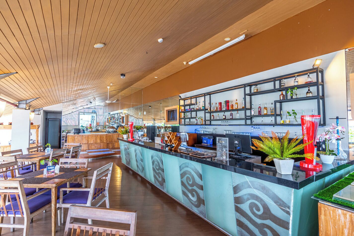 A bar area with a counter, shelves with bottles, and seating with tables and chairs.