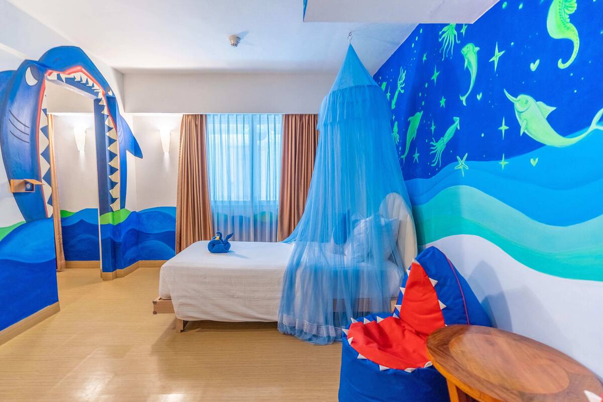 A room with a bed, a canopy, and a mural of sea creatures.