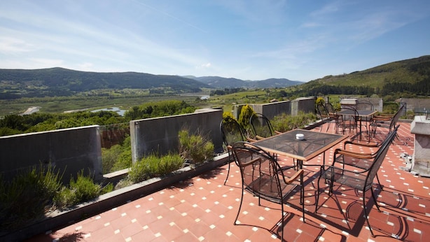 An outdoor terrace with a table and chairs, overlooking a valley and hills. - Castillo de Arteaga (Gautegiz Arteaga)