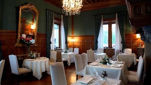A dining room with multiple tables set for service, wooden paneled walls, and a chandelier. - Castillo de Arteaga (Gautegiz Arteaga)