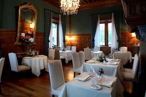A dining room with multiple tables set for service, wooden paneled walls, and a chandelier. - Castillo de Arteaga (Gautegiz Arteaga)