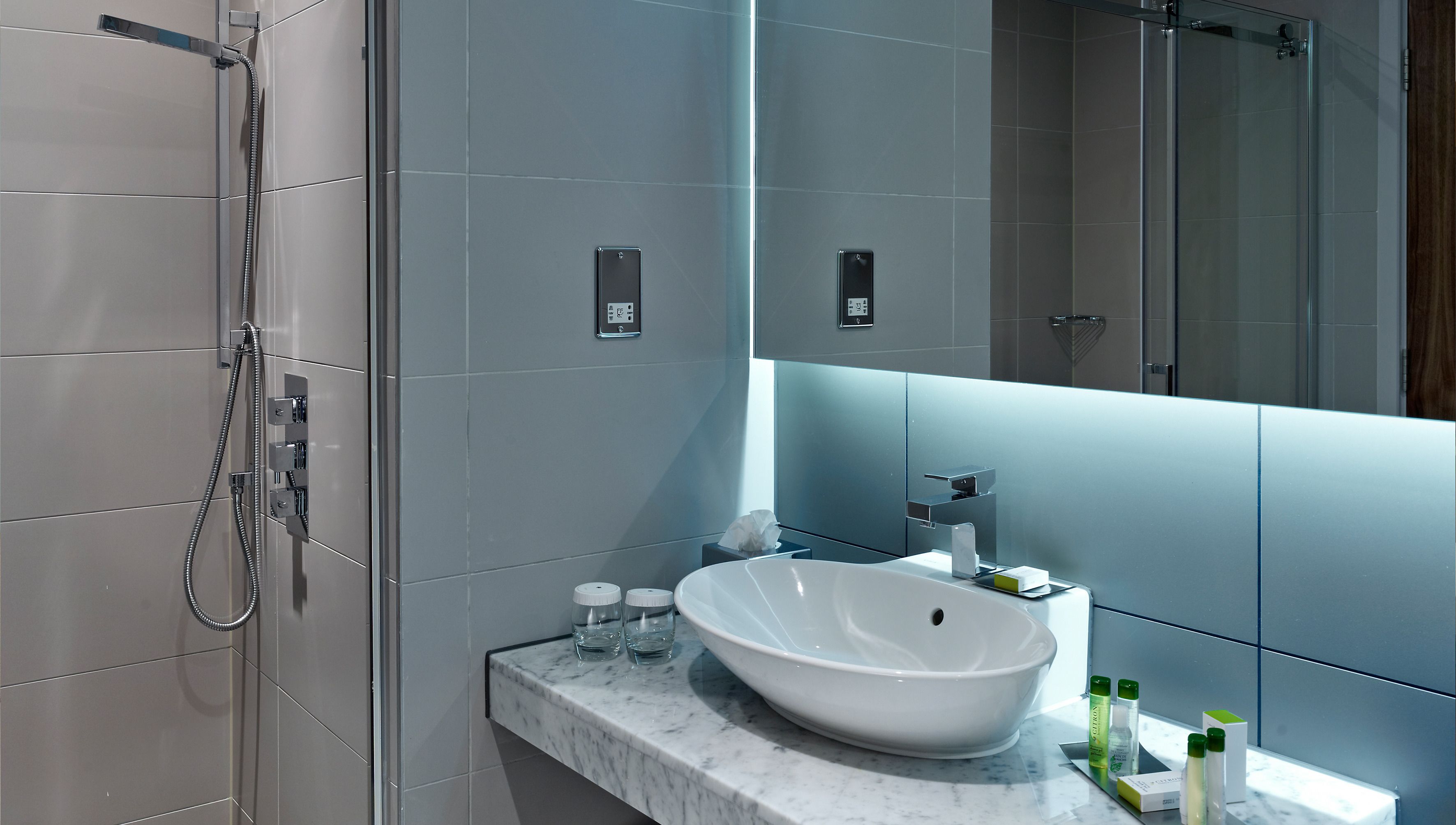 Une salle de bain moderne avec une douche à l’italienne en verre, un lavabo blanc et un plan de toilette en marbre.