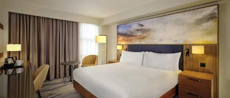 Habitación de hotel con una cama grande, mesitas de noche, un escritorio con silla, una pequeña mesa redonda y un cuadro abstracto de gran tamaño en la pared.